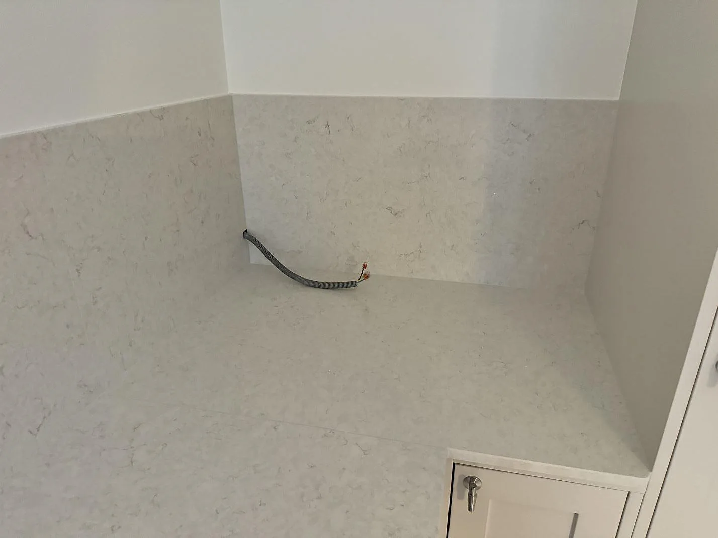Bänkskiva och stänkskydd i polerad Silestone Snowy Ibiza i en köksnisch i MALMÖ, med synlig eldragning under montering.