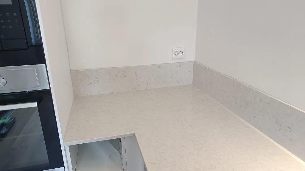 Hörnsektion med polerad Silestone Snowy Ibiza, låg stänkkant och släta vita väggar bredvid svart ugnspelare i Malmö.