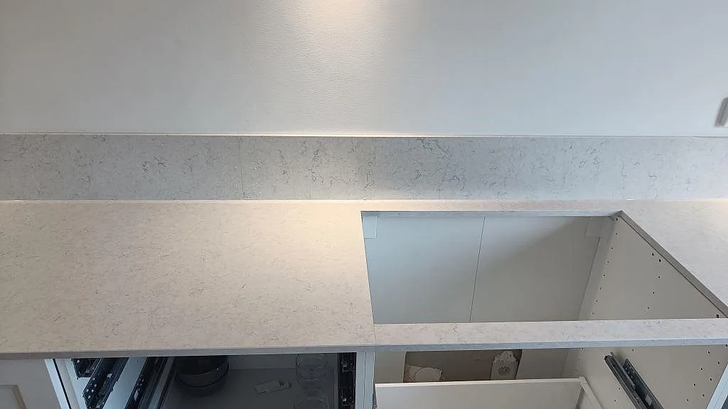 Köksbänkskiva i polerad Silestone Snowy Ibiza med rektangulärt urtag för häll och stänkkant mot vit vägg i Malmö.