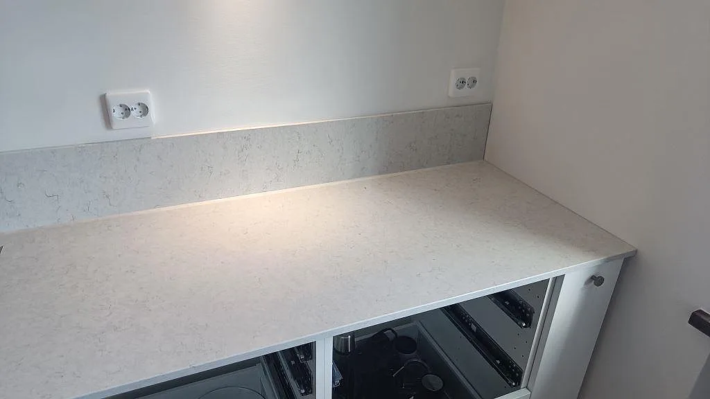 Rak arbetsyta i polerad Snowy Ibiza komposit med låg stänkkant, vita köksstommar och svarta detaljer i Malmö.