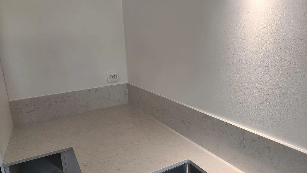 Hörnvy av polerad Silestone Snowy Ibiza med stänkkant, vit vägg och rostfri underlimmad diskho i kök i Malmö.