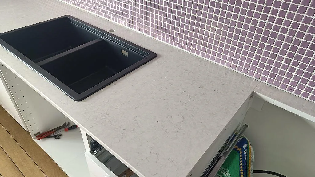 Detalj av polerad Silestone Snowy Ibiza bänkskiva med svart dubbelho, ljus stenådring och lila mosaik i ett kök i Malmö.