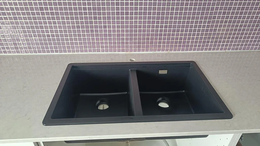 Närbild på svart dubbelho i en polerad Silestone Snowy Ibiza bänkskiva med ljus komposityta och mosaikvägg i Malmö.