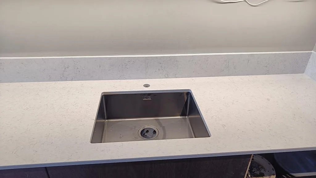 Närbild på rostfri diskho i en polerad Silestone Snowy Ibiza-köksbänkskiva med ljus stenådring i Malmö.