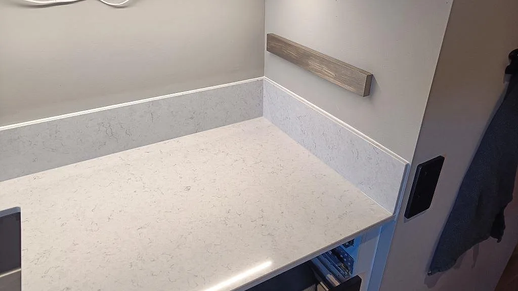 Hörn av köksbänkskiva i polerad Silestone Snowy Ibiza med låg stänkkant och öppen stomme under montering i Malmö.