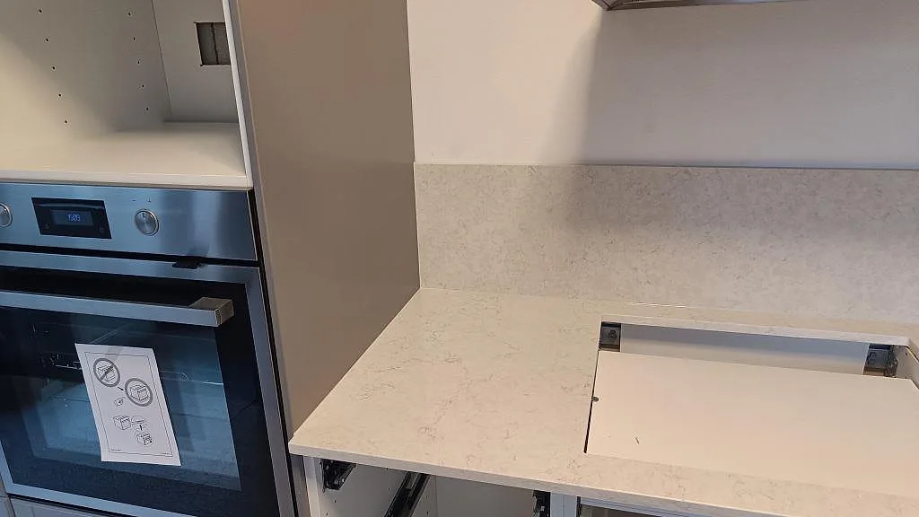 Vänster bänkskiva i Silestone Snowy Ibiza med förberett hällurtag intill ugn och matchande stänkskydd i ett Malmö-kök under montering.
