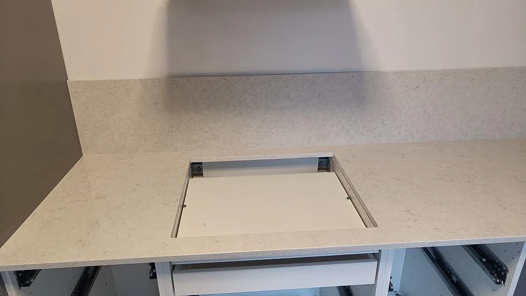 Närbild på hällurtag i polerad Silestone Snowy Ibiza, ljus kompositbänkskiva med öppna köksstommar under montering i Malmö.