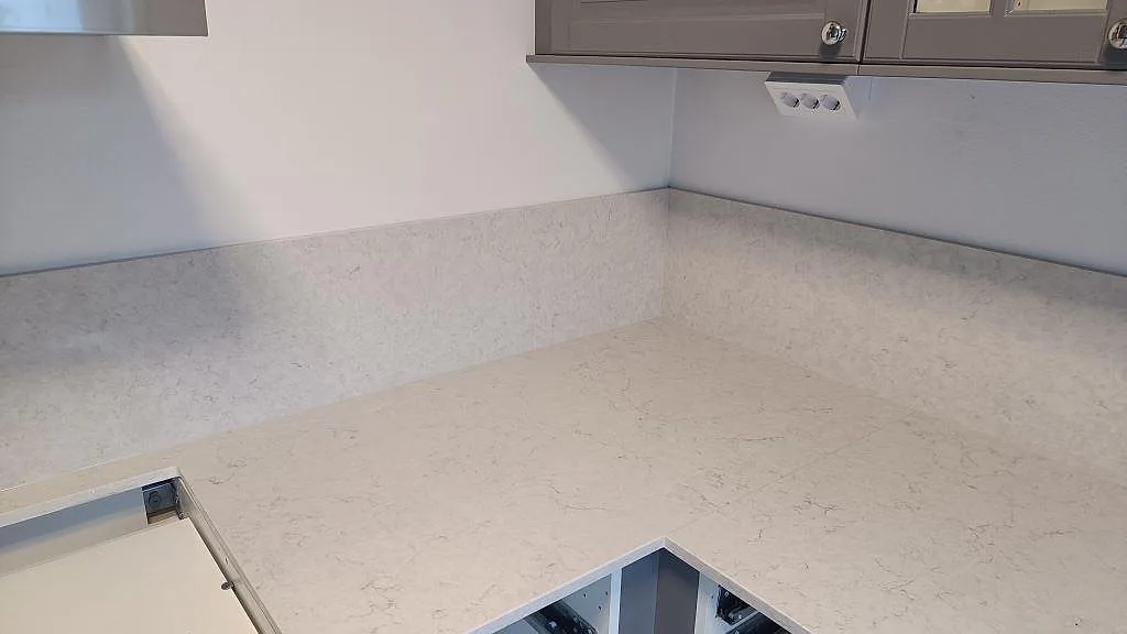 Hörnparti av köksbänkskiva och stänkskydd i polerad Silestone Snowy Ibiza, ljus kvartskomposit med mjuk grå teckning i Malmö.