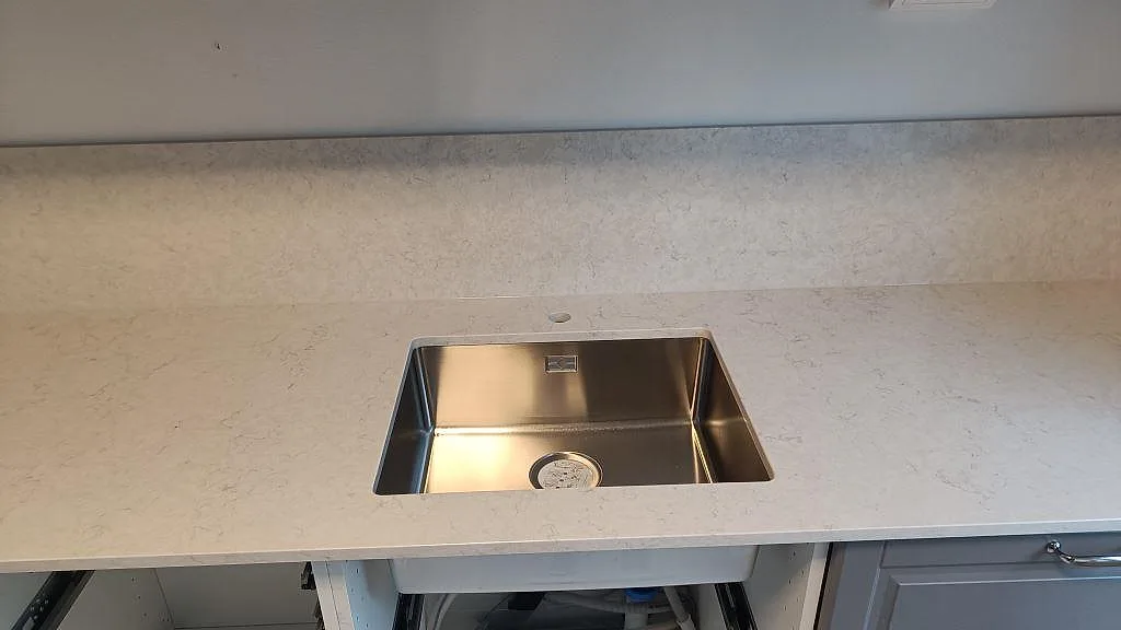Rostfri diskho i en polerad köksbänkskiva av Silestone Snowy Ibiza med ljus kvartskomposit och lågt stänkskydd i Malmö.