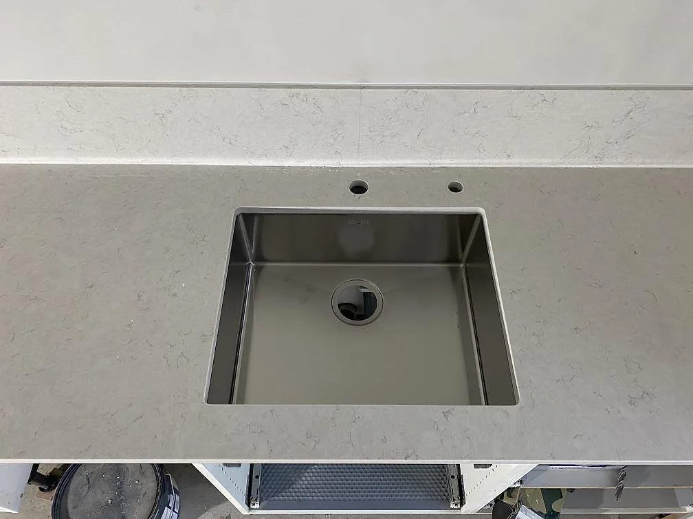 Underlimmad rostfri diskho i polerad Silestone Snowy Ibiza med två borrade hål för blandare i ett kök i Malmö.