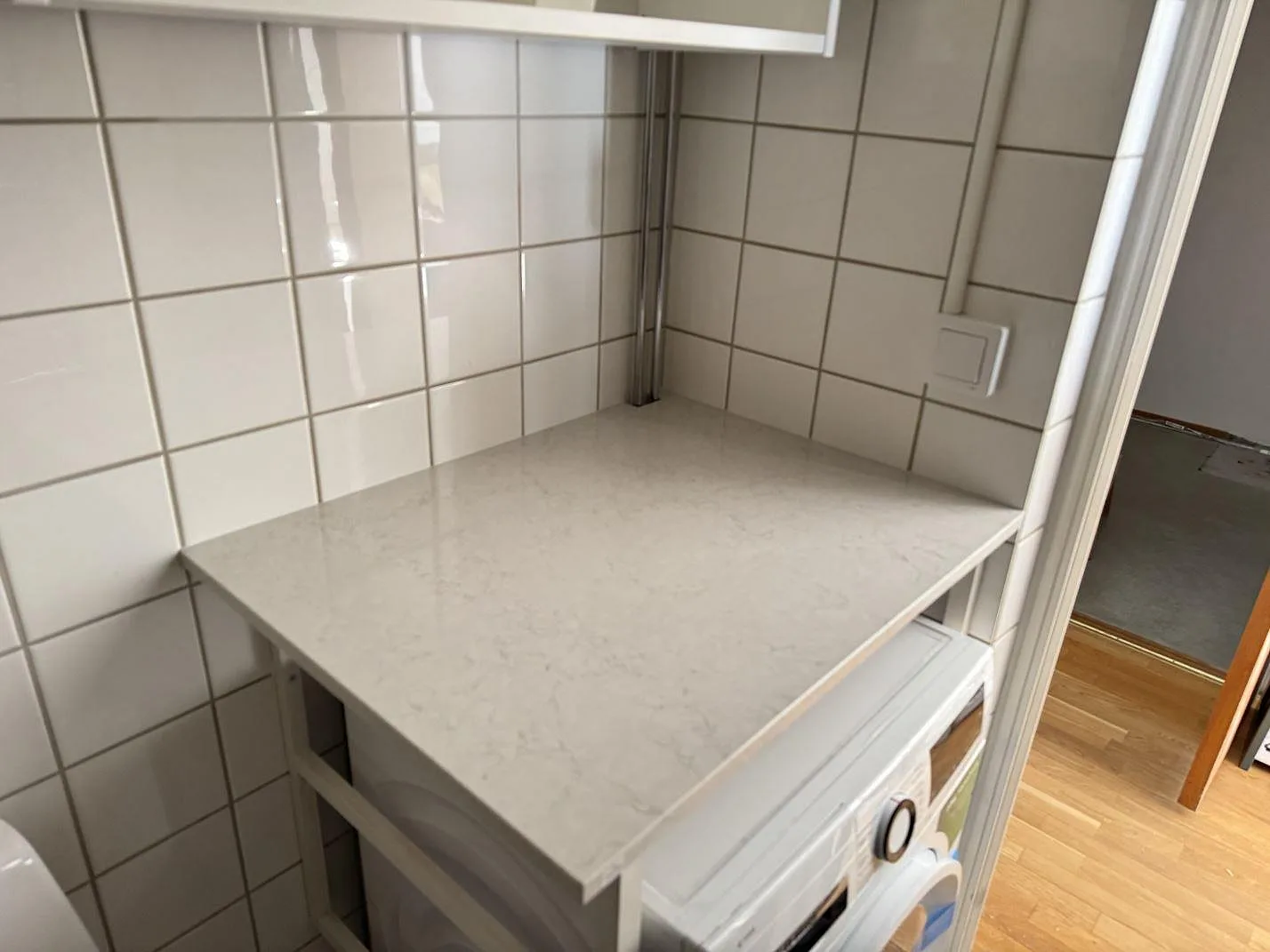 Sidobänk i polerad Silestone Snowy Ibiza monterad i en kaklad nisch i Malmö.