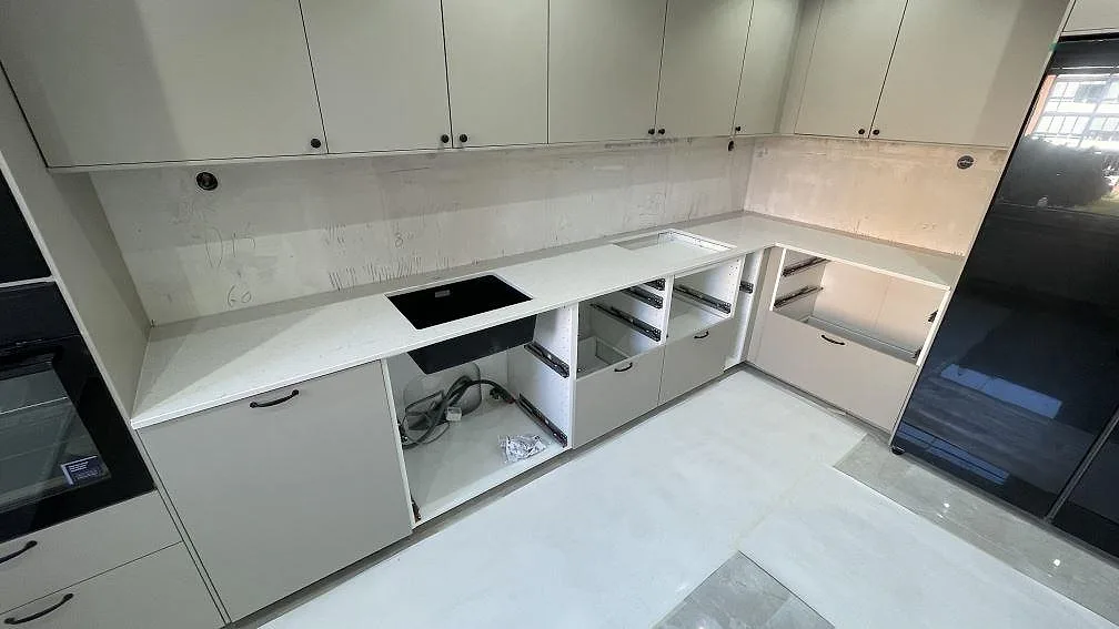 L-formad köksbänkskiva i polerad Silestone Snowy Ibiza, vit kvartskomposit, med låg stänkkant och svart diskho i Malmö.