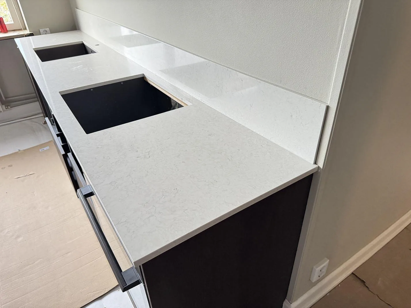 Polerad Silestone Snowy Ibiza som lång köksbänkskiva med uppvikt stänkskydd och två öppningar under montering i Malmö.