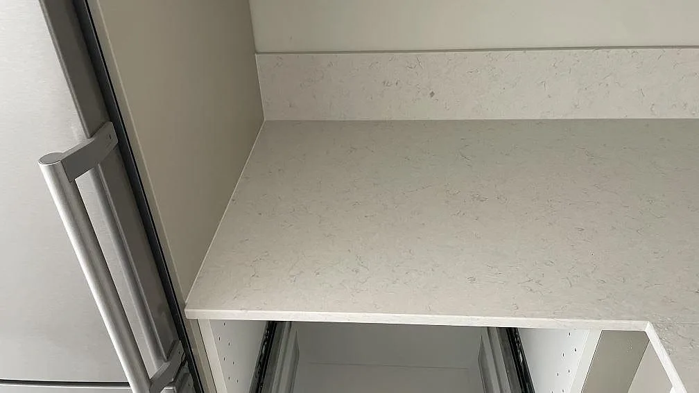 Väggbänk i polerad Silestone Snowy Ibiza med låg stänkkant i samma sten vid kylskåpet, vit kvartskomposit i ett kök i Malmö.