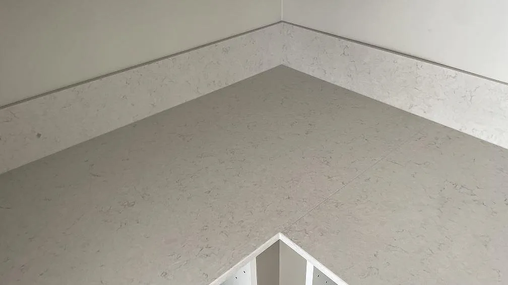 Hörnparti av köksbänkskiva och stänkkant i polerad Silestone Snowy Ibiza, med ljus grå ådring i ett kök under montering i Malmö.