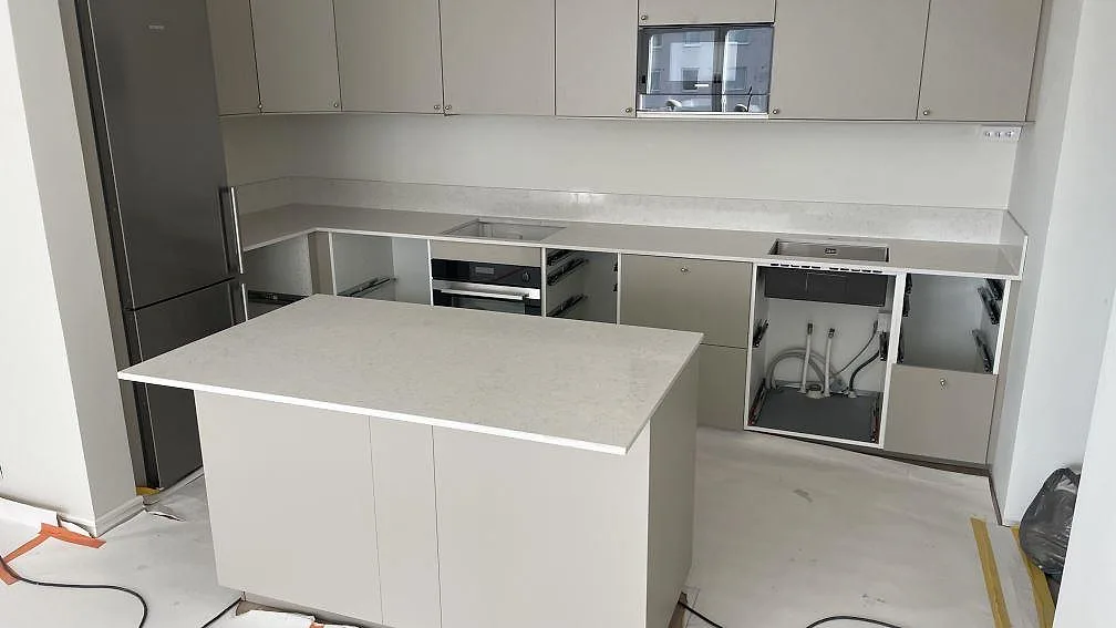 Köksbänkskiva och köksö i vit Silestone Snowy Ibiza, polerad kvartskomposit, med låg stänkkant och öppna köksstommar under montering i Malmö.