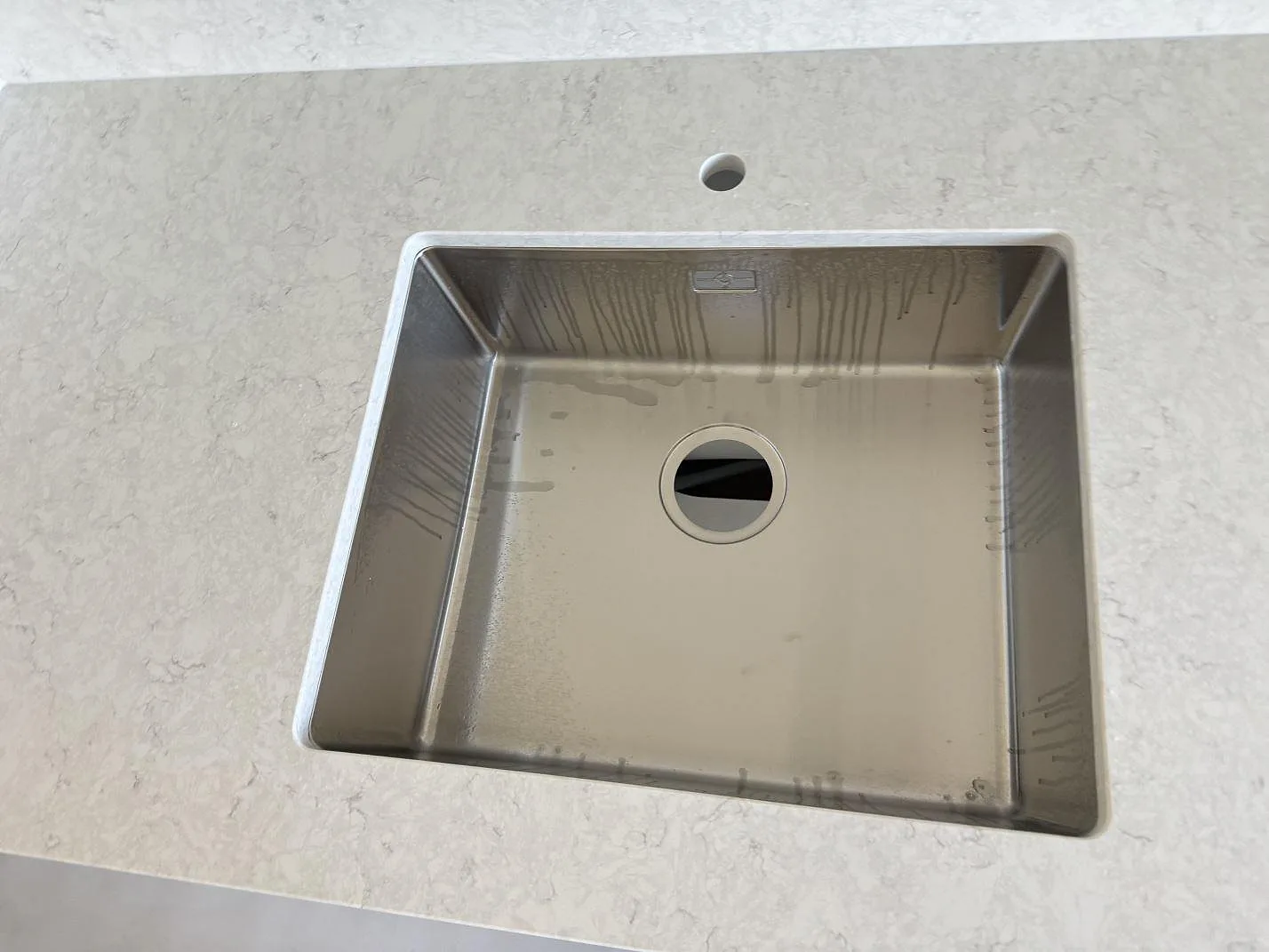 Närbild på underlimmad rostfri diskho och blandarhål i polerad Silestone Snowy Ibiza, kvartskomposit, i Malmö.