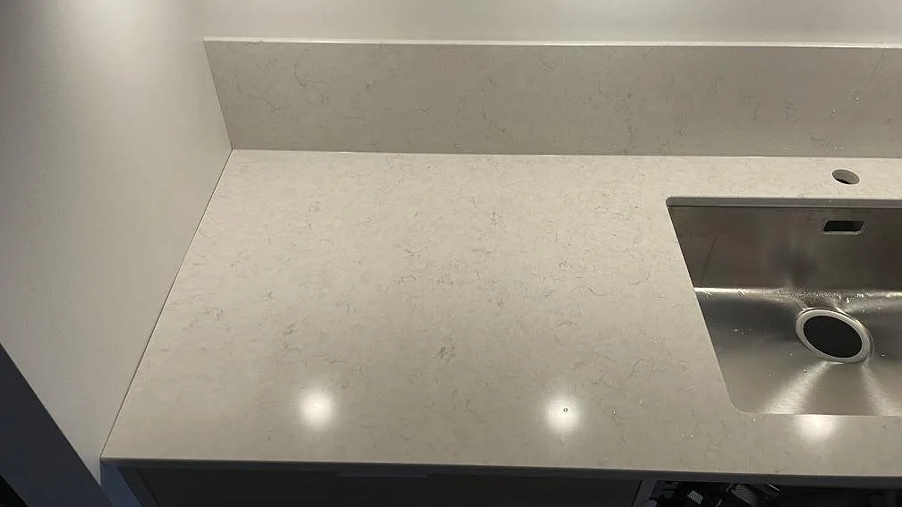 Detalj av polerad Silestone Snowy Ibiza-bänkskiva med rostfri diskho, blandarhål och uppvikt stänkskydd i ett kök i Malmö.