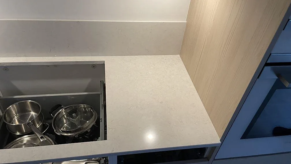 Sidovy av hällöppning och arbetsyta i polerad Silestone Snowy Ibiza, ljus kvartskomposit intill högskåp i ett kök i Malmö.