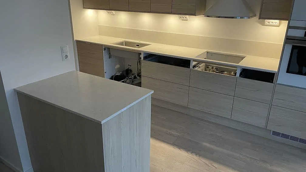 Köksbänkskiva och köksö i polerad Silestone Snowy Ibiza, ljus kvartskomposit, med rostfri diskho, hällöppning och stänkskydd i ett kök i Malmö.