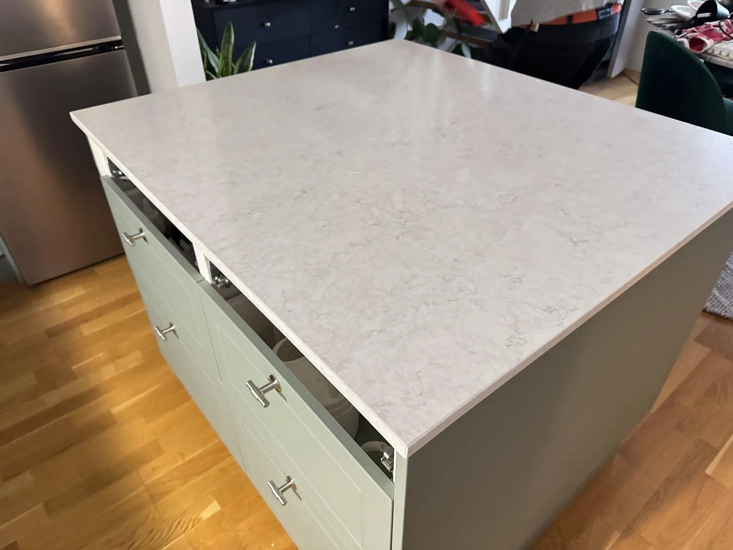 Närbild av den polerade Silestone Snowy Ibiza-bänkskivan på köksön, med ljus kompositådring och gröna köksluckor i Malmö.