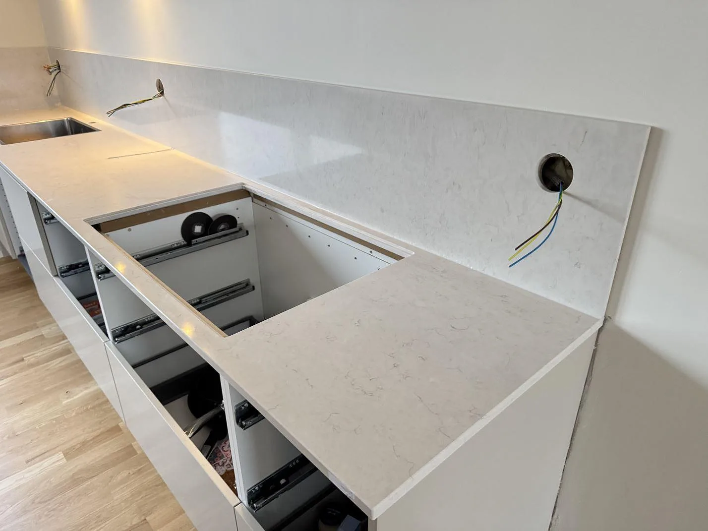 Lång L-formad köksbänk i vit Silestone Snowy Ibiza under montering, med underlimmad rostfri diskho, tom hålurtagning för häll och dragna elledningar i ett kök i Malmö.