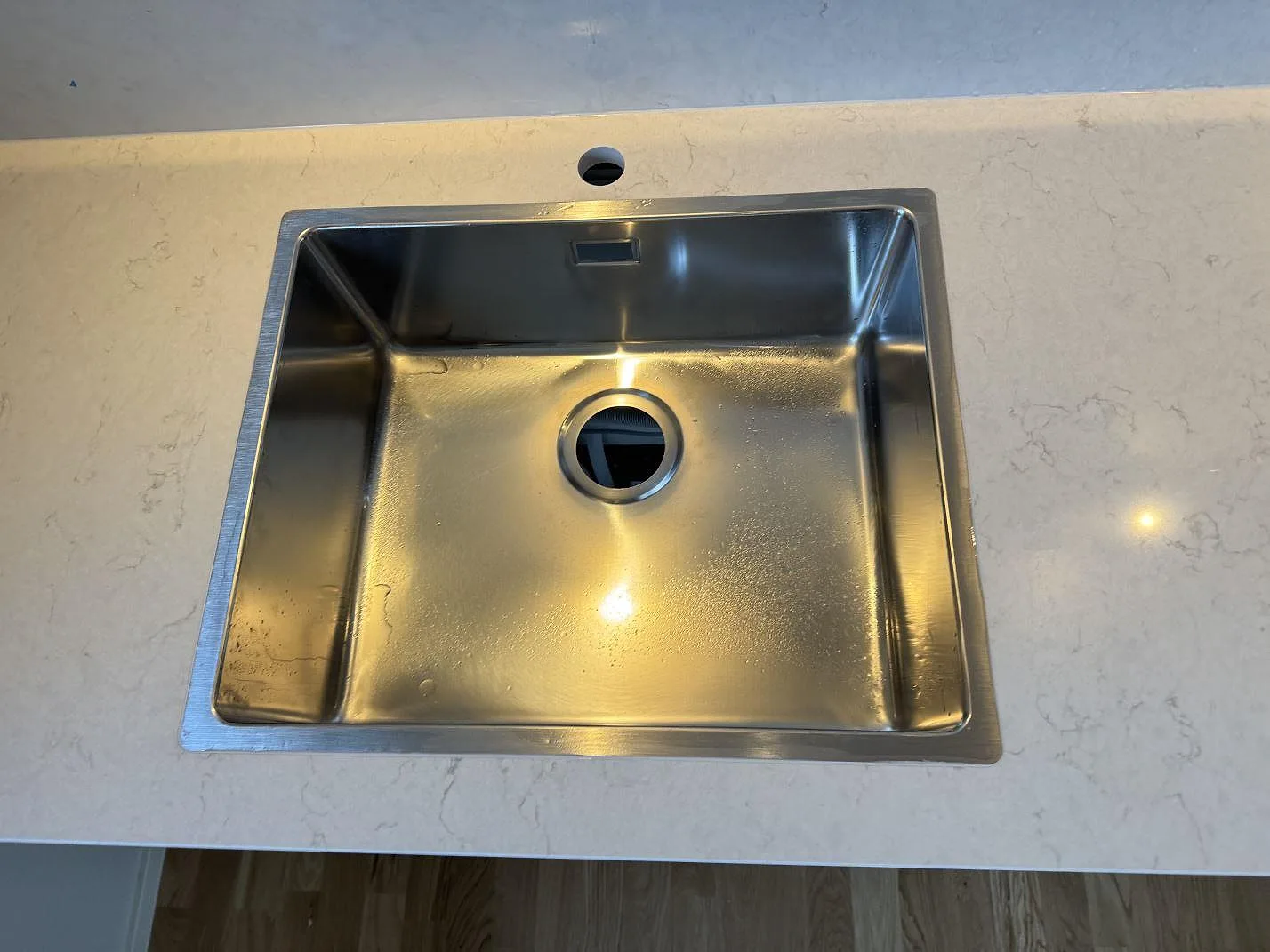 Närbild ovanifrån på underlimmad rostfri diskho i vit Silestone Snowy Ibiza med diskret ådring och borrat hål för blandare i ett kök i Malmö.