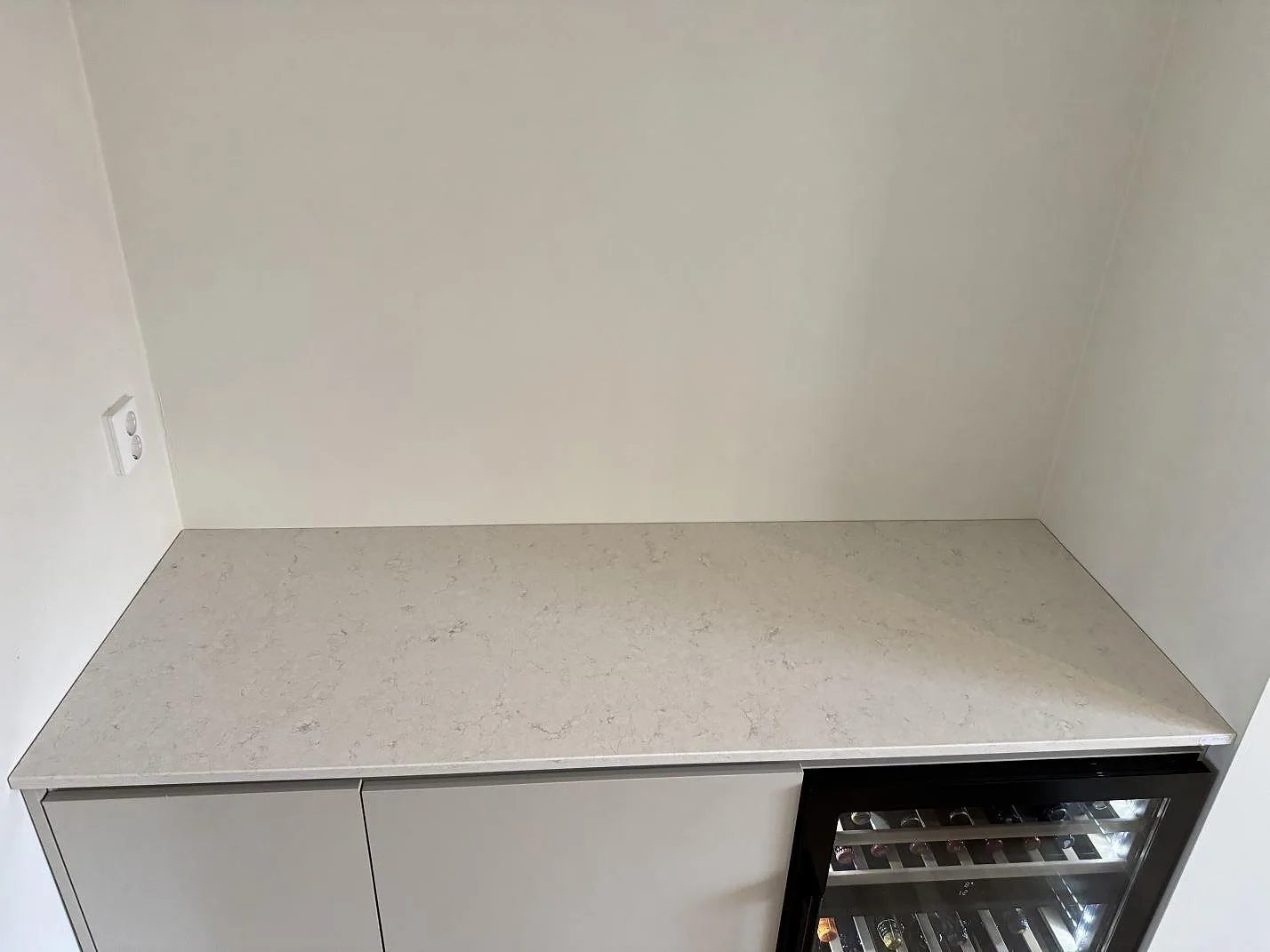 Köksbänkskiva i vit Silestone Snowy Ibiza, polerad komposit, monterad mot vägg med vinkyl inbyggd nedanför i ett kök i Malmö.