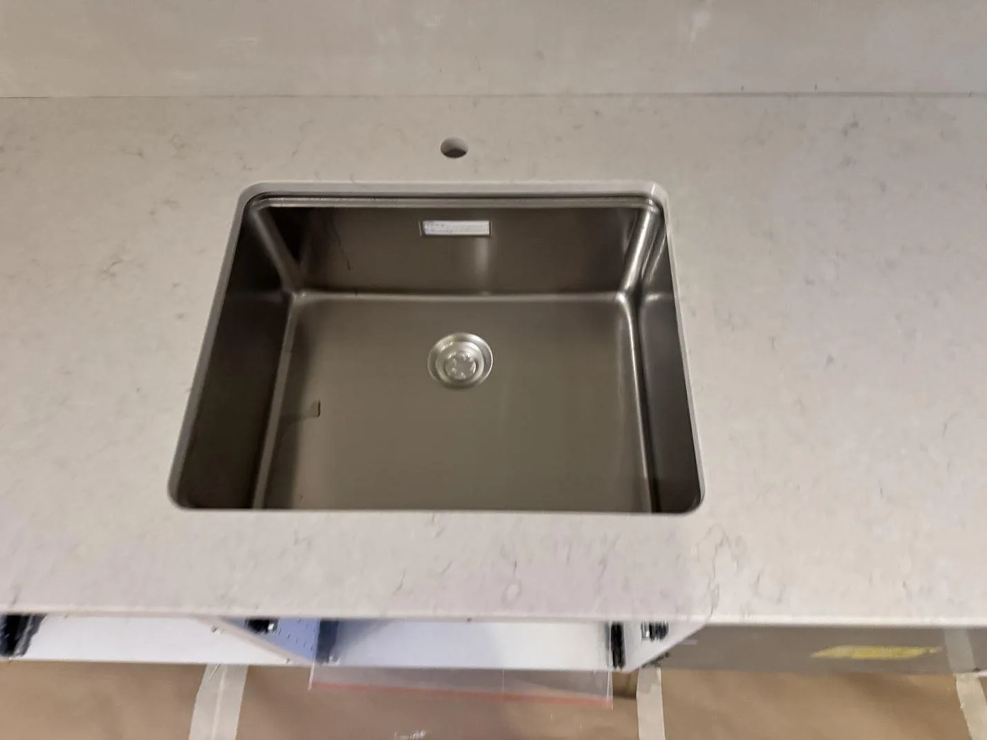 Underlimmad rostfri diskho i en vit Silestone Snowy Ibiza-köksbänkskiva med kranhål, sett uppifrån i ett kök i Malmö.