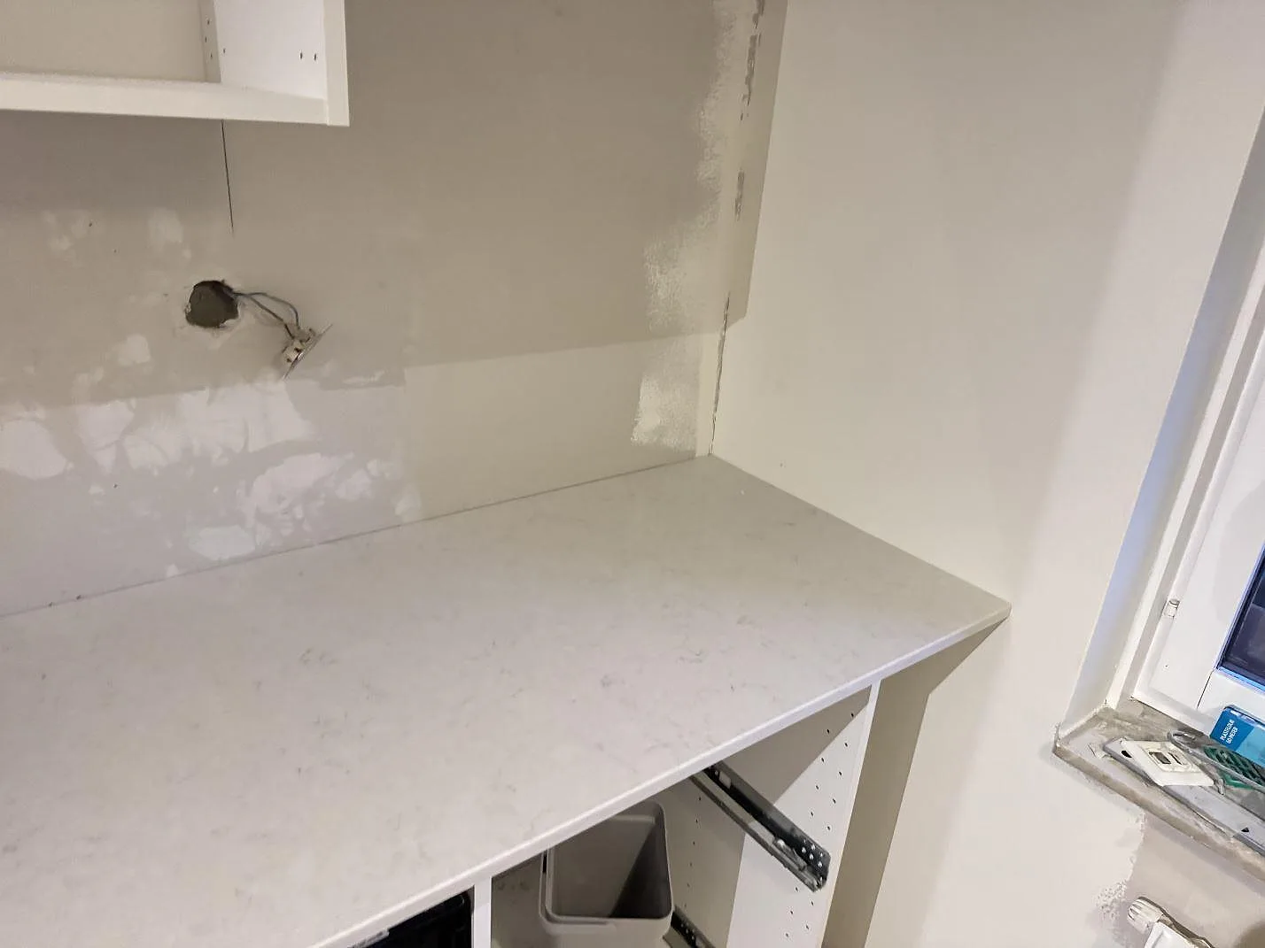 Vit polerad Silestone Snowy Ibiza-köksbänkskiva i ett hörn vid fönstret, med diskret ådring, i ett kök under montering i Malmö.