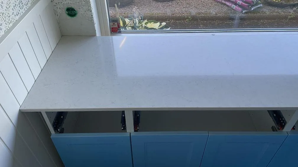 Lång köksbänkskiva i polerad Silestone Snowy Ibiza med ljus ådring och öppna underskåp i Mellbystrand.
