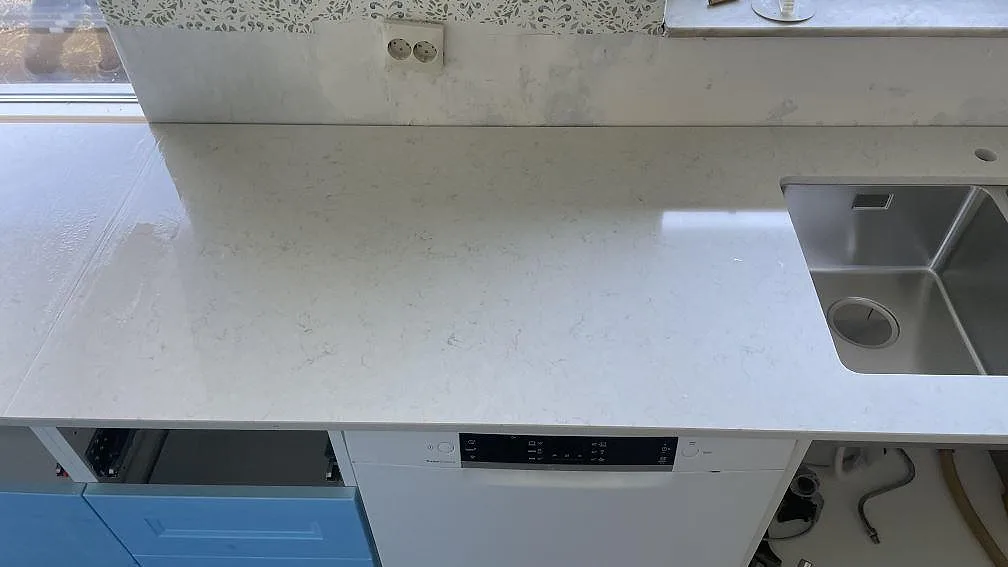 Polerad Silestone Snowy Ibiza bänkskiva med diskhoområde och diskmaskin i ett kök under montering i Mellbystrand.