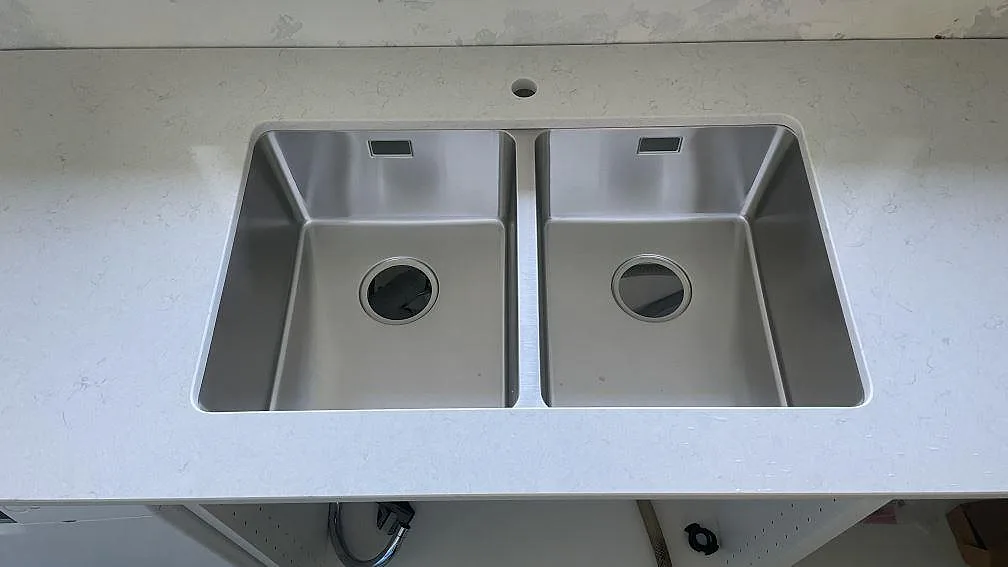 Rostfri dubbel diskho i en vit polerad Silestone Snowy Ibiza köksbänkskiva under montering i Mellbystrand.