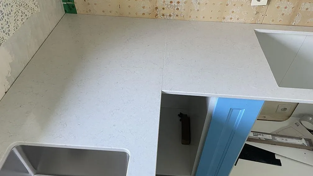 L-formad köksbänkskiva i vit Silestone Snowy Ibiza, polerad kvartskomposit, med synlig hörnpassning i Mellbystrand.