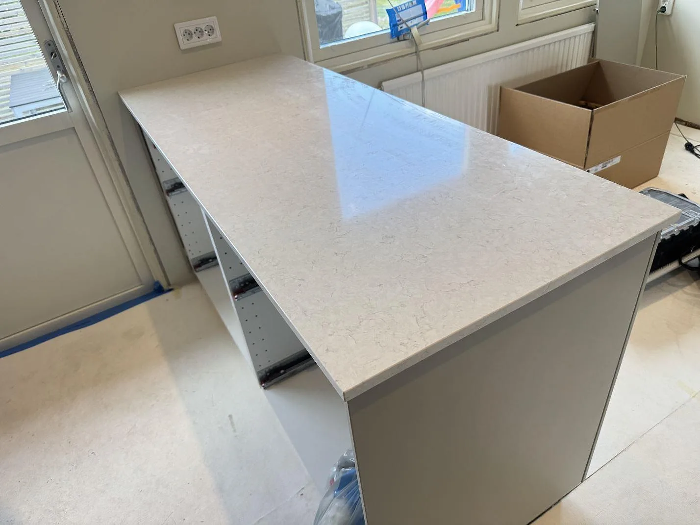 Köksbänkskiva i polerad Silestone Snowy Ibiza, ljus kvartskomposit, monterad på köksstommar vid fönster i Mörrum.