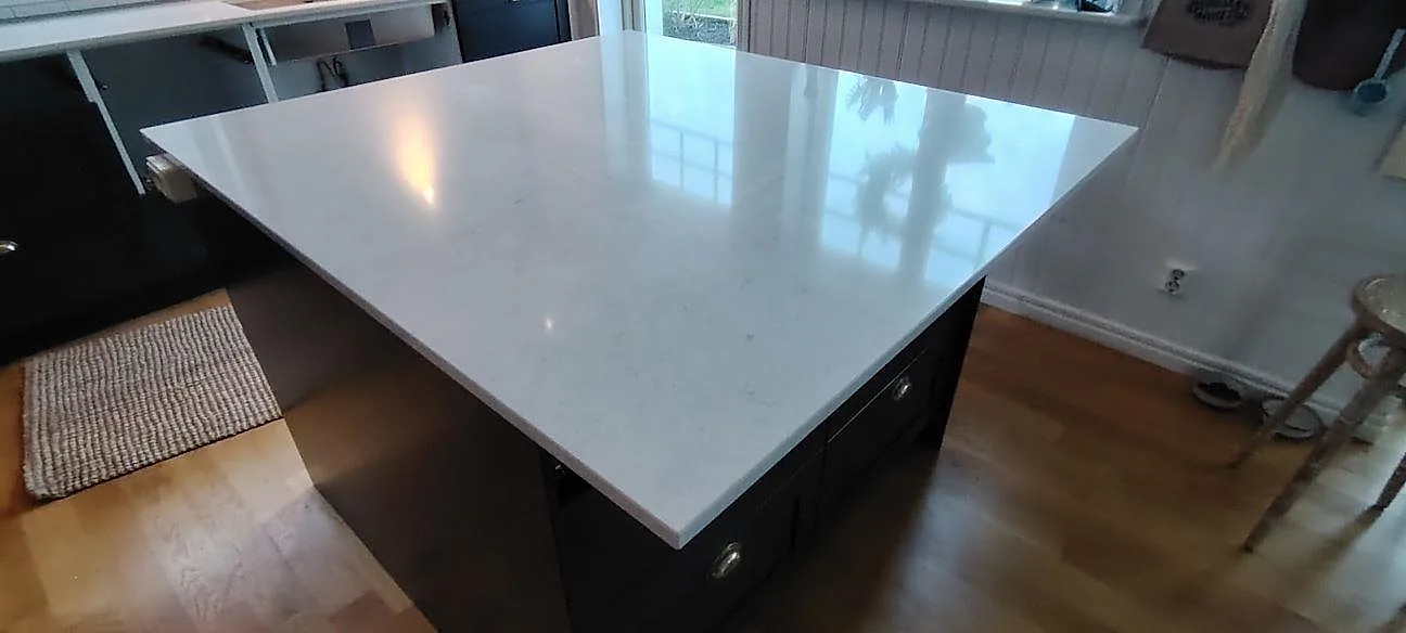 Närbild av polerad Silestone Snowy Ibiza kvartskomposit på köksö med ljus ådring och speglingar från fönster i Motala.