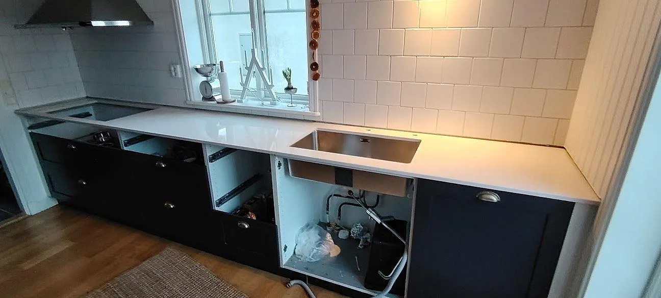Väggmonterad köksbänkskiva i polerad Silestone Snowy Ibiza kvartskomposit med synlig diskho mot vit kakelvägg i Motala.