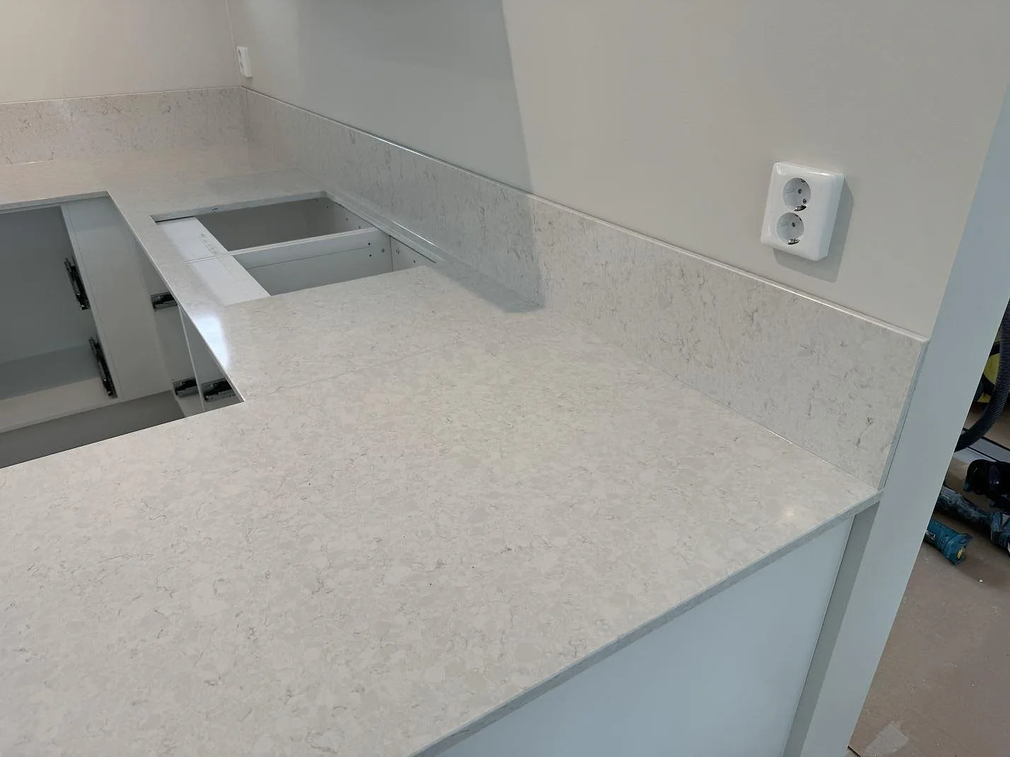 Hörnvy av polerad Silestone Snowy Ibiza bänkskiva med rektangulär öppning och låg stänkkant i köket i Nättraby.