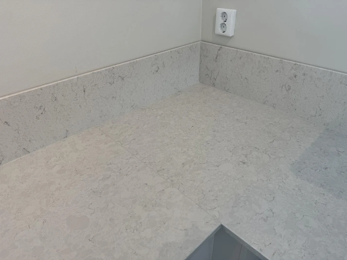 Närbild av hörn i polerad Silestone Snowy Ibiza, med ljus kvartskompositbänk och låg stänkkant runt väggarna i Nättraby.