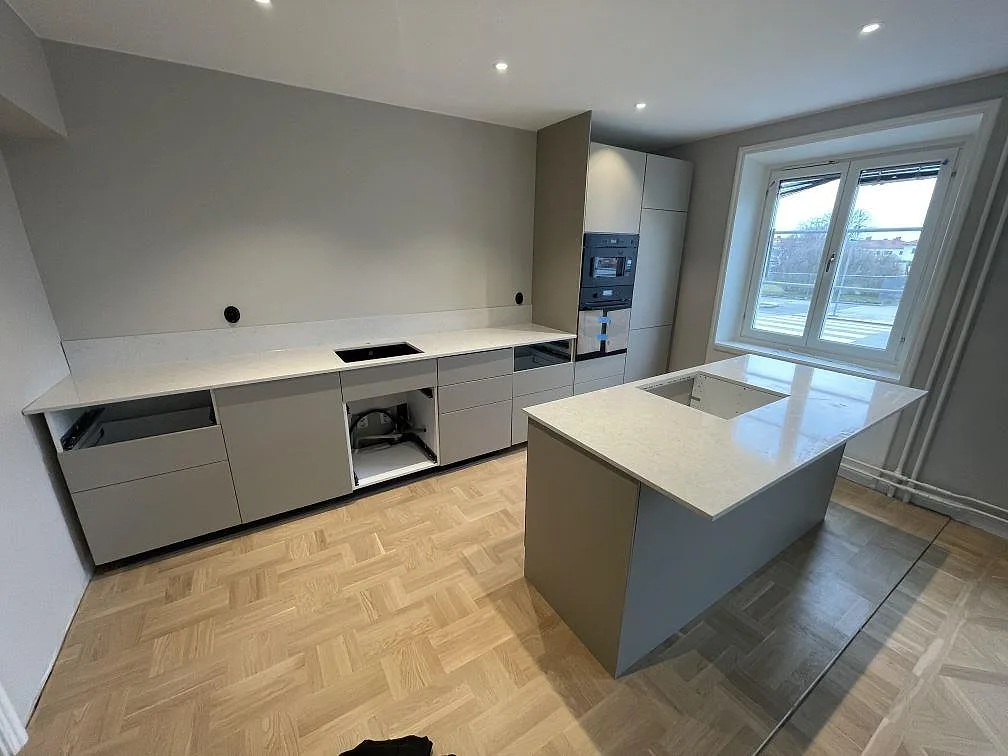 Bred vy över kök i Norrköping med polerad Silestone Snowy Ibiza på köksö, bakre bänkrad och 12 mm stänkskydd.