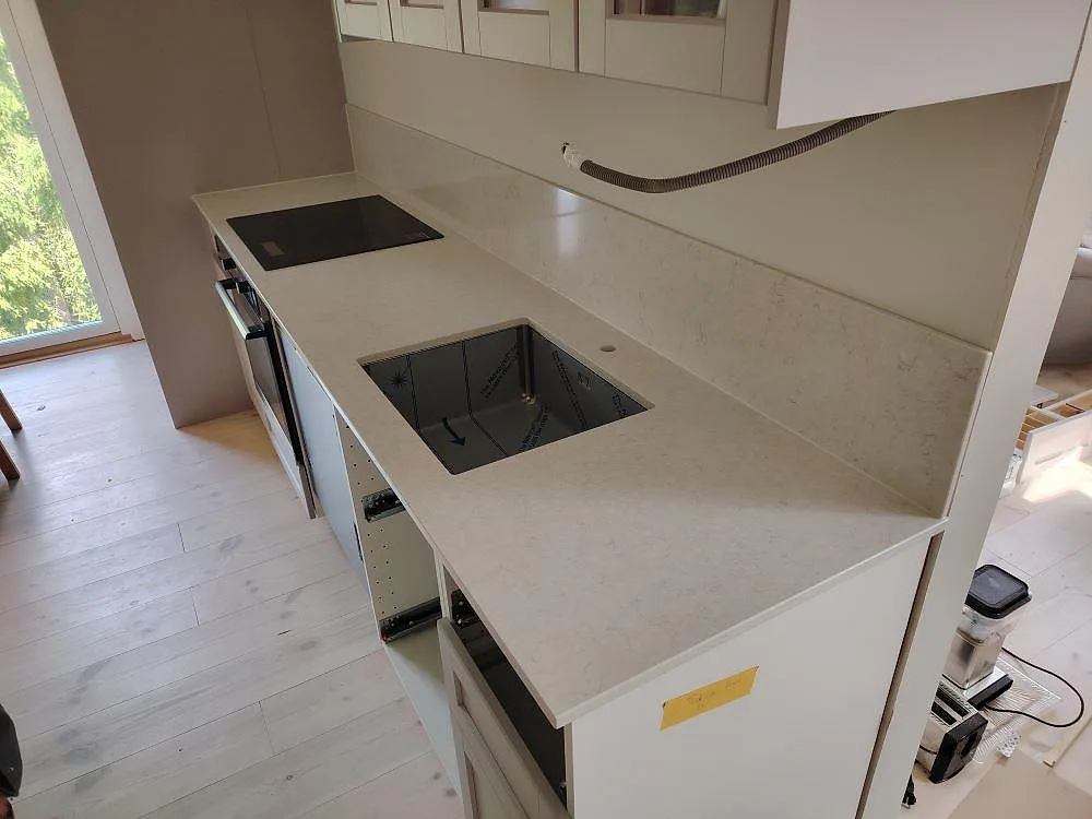 Polerad Silestone Snowy Ibiza som köksbänkskiva med svart diskho, häll och uppvikt stänkskydd i Nyköping.