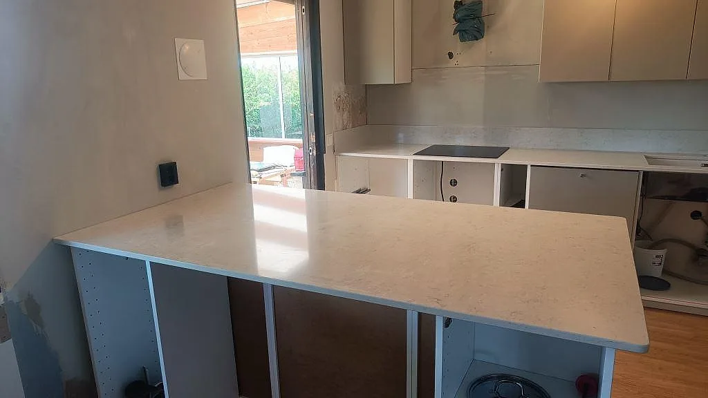 Köksbänkskiva i polerad Silestone Snowy Ibiza med peninsula och vit köksinredning under montering i Önnestad.