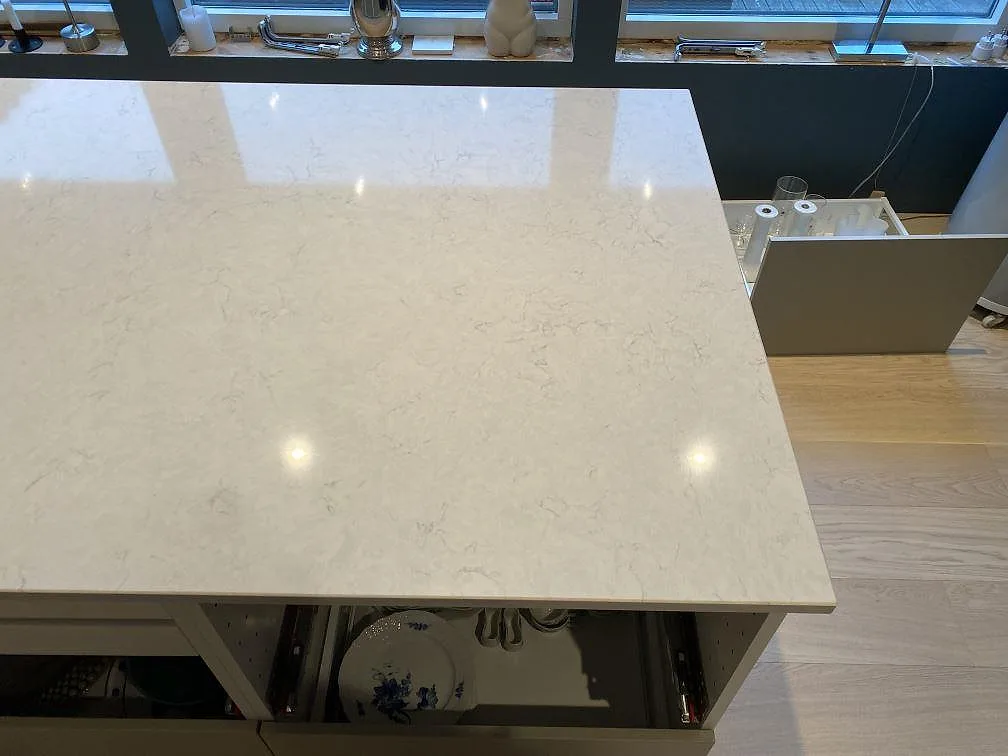 Polerad köksö i vit Silestone Snowy Ibiza med mjuk grå ådring, närbild på hörnet med öppet skåp under, i ett kök i Österskär.