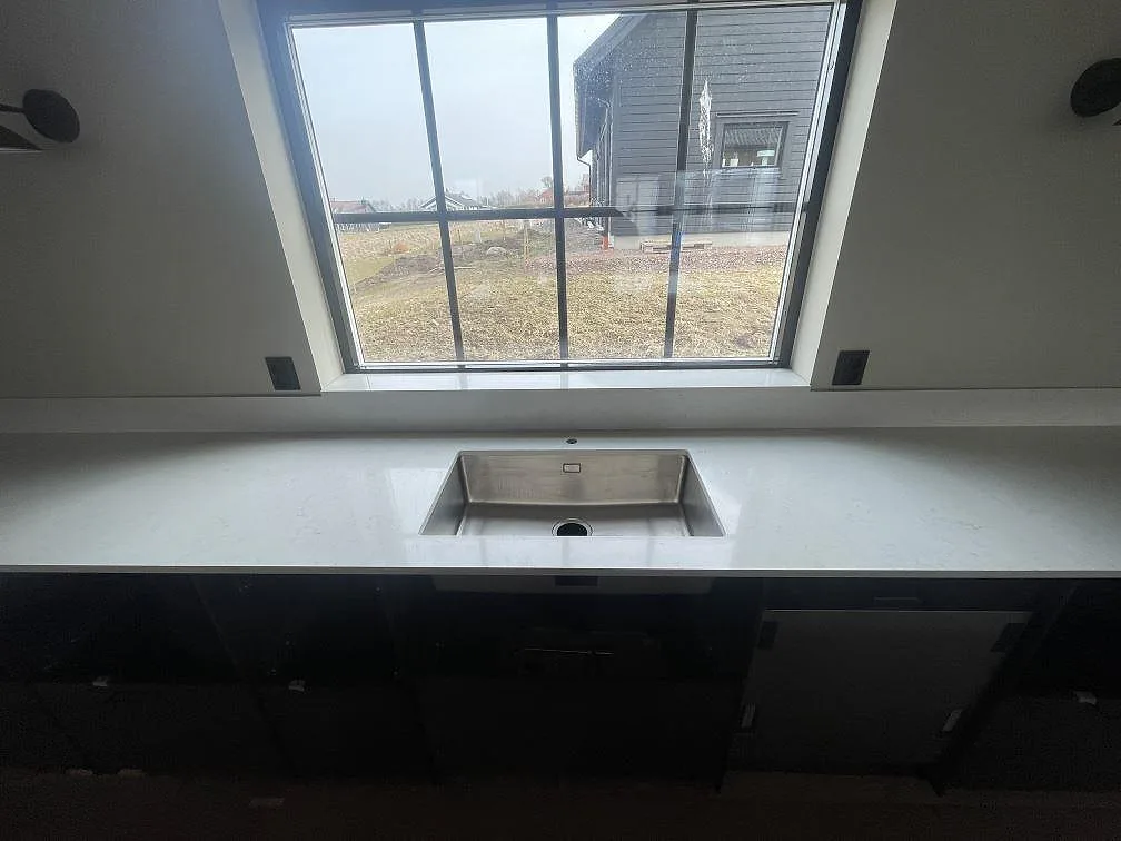 Underlimmad rostfri diskho i vit Silestone Snowy Ibiza, polerad bänkskiva under fönstret i ett kök i Östra Karup.