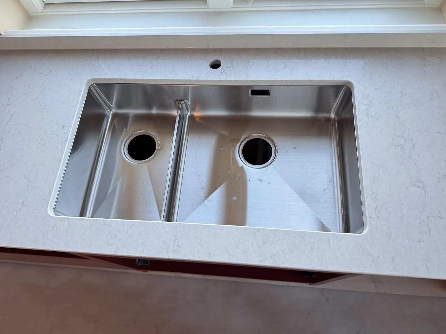 Underlimmad rostfri diskho med dubbla hoar i en matt vit Silestone Snowy Ibiza-bänkskiva, sedd ovanifrån, i ett kök i Östra Vemmerlöv.