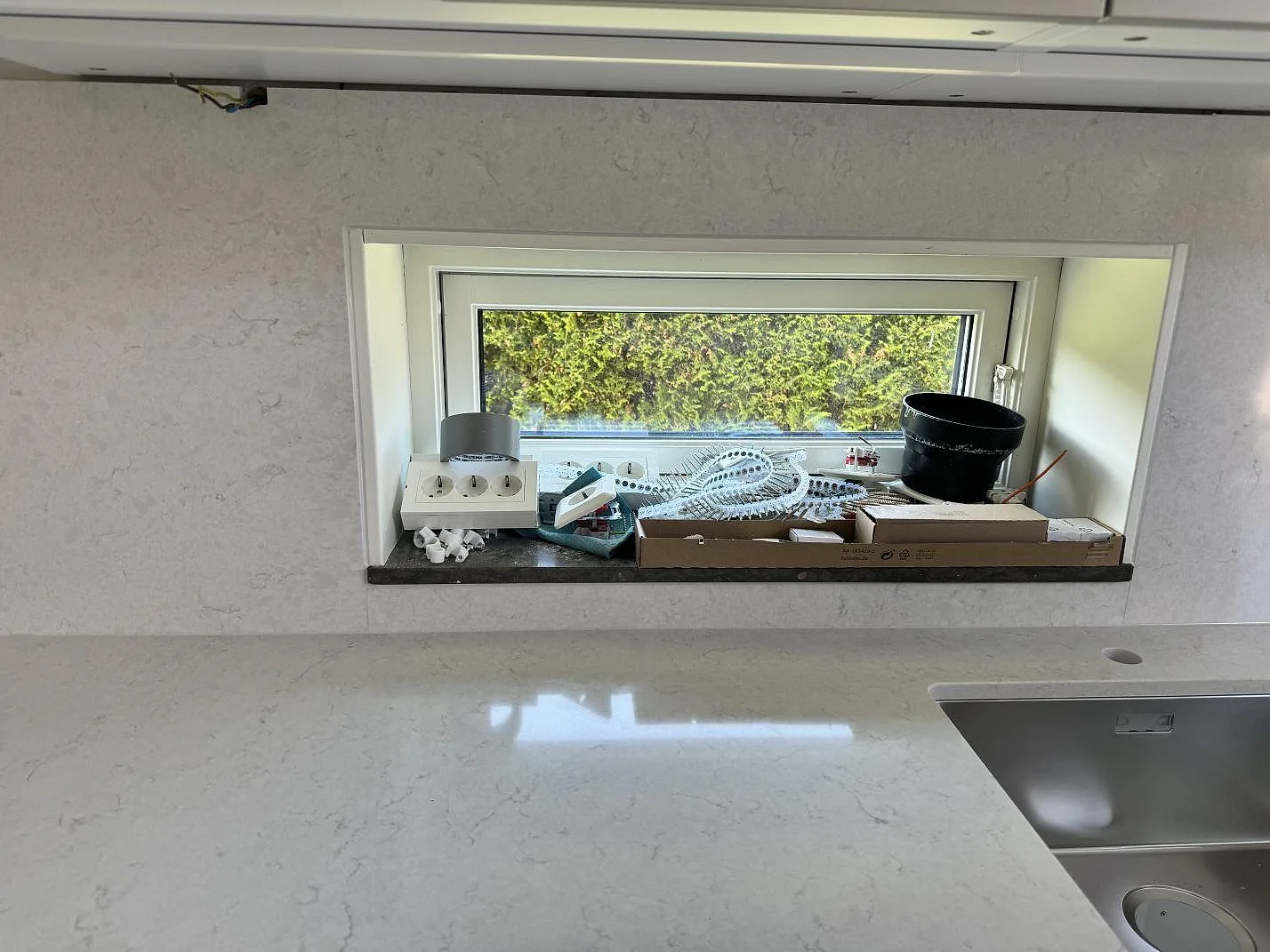 Silestone Snowy Ibiza som polerad bänkskiva och väggbeklädnad runt köksfönster med rostfri diskho i Ojersjo.