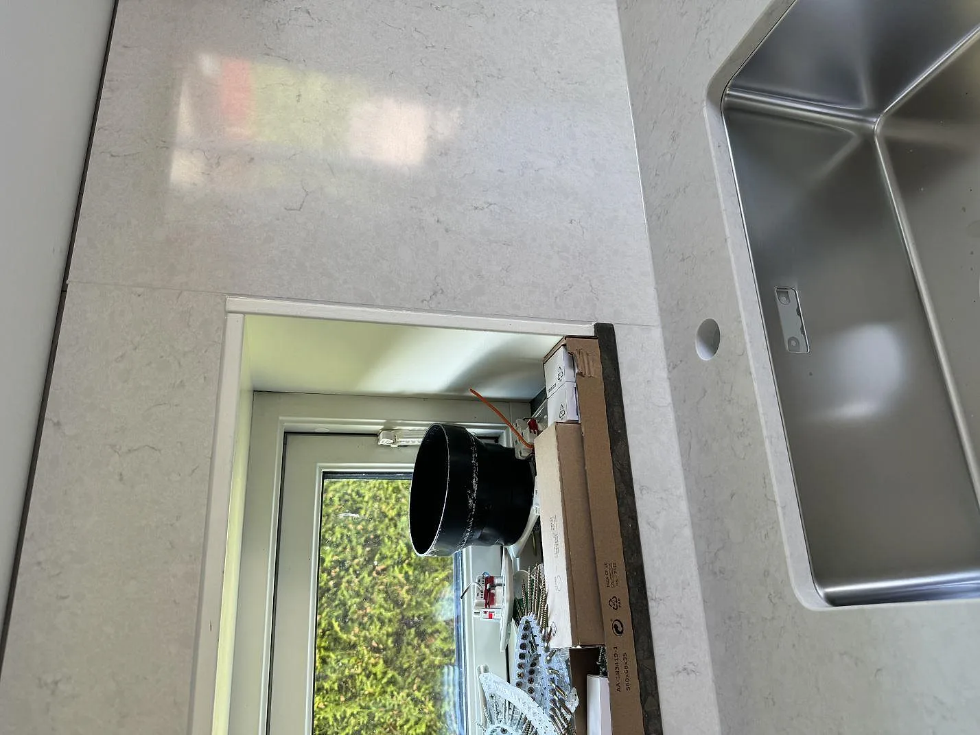 Detalj av polerad Silestone Snowy Ibiza runt fönsternisch och rostfri diskho under montering i Ojersjo.