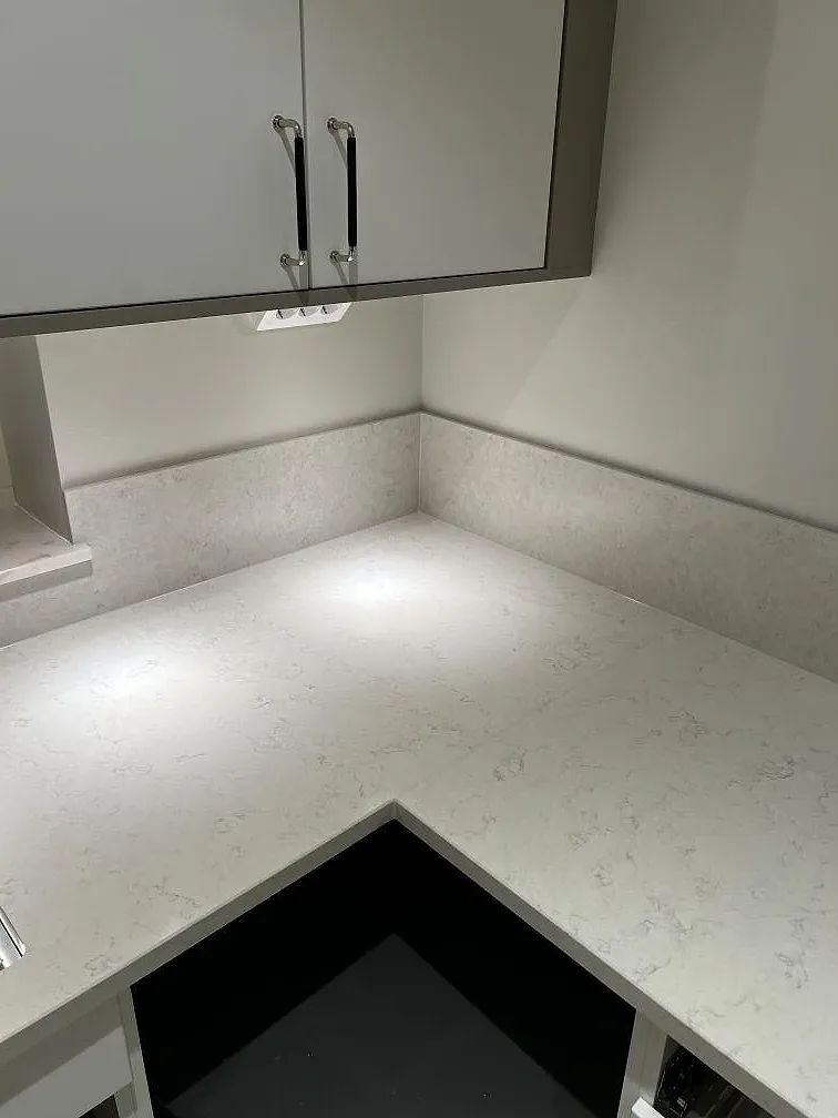 Köksbänkskiva i Silestone Snowy Ibiza med uppvikt stänkkant i samma sten och infälld induktionshäll i ett kök i Olofstorp.