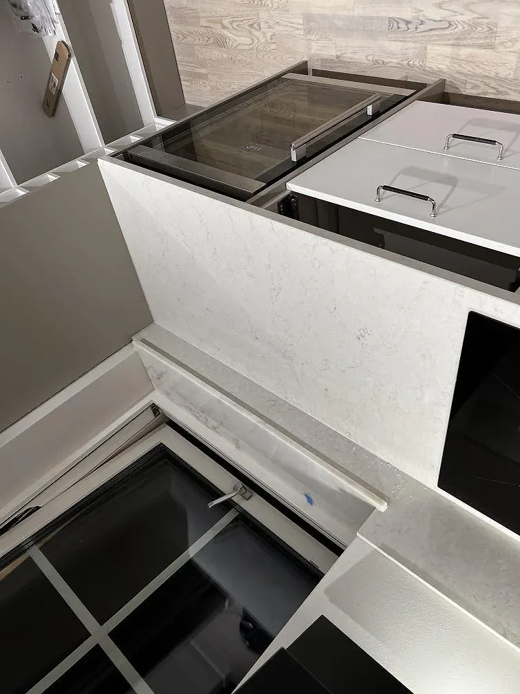 Polerad köksbänkskiva i vit Silestone Snowy Ibiza vid fönstret, med induktionshäll och inbyggd ugn, i ett kök i Olofstorp.