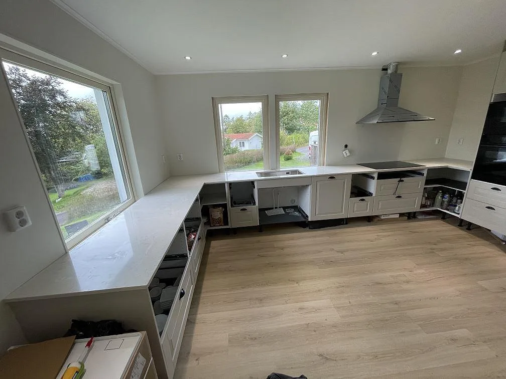 L-format kök i Olofstorp med polerad Silestone Snowy Ibiza, 20 mm kvartskomposit, stora fönster och svart induktionshäll.